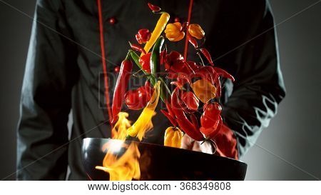 Closeup of chef throwing chilli peppers mix from wok pan in fire. Fresh asian food preparation on dark background.
