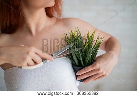 Faceless Red-haired Caucasian Woman Wrapped In A White Terry Towel Shears A Potted Plant With Scisso