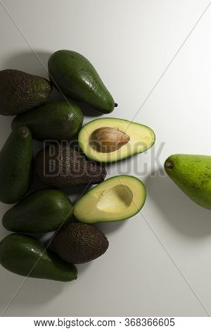 Sliced And Whole Avocado Fruits Of Different Varieties Of Green And Brown On A Light Background.