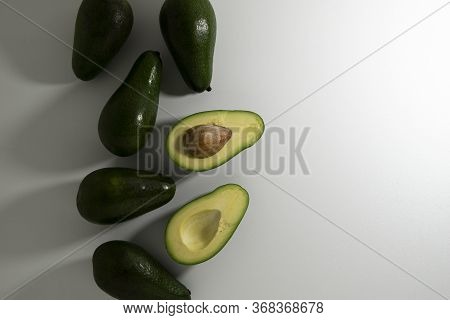 Sliced And Whole Avocado Fruits Of Different Varieties Of Green And Brown On A Light Background.
