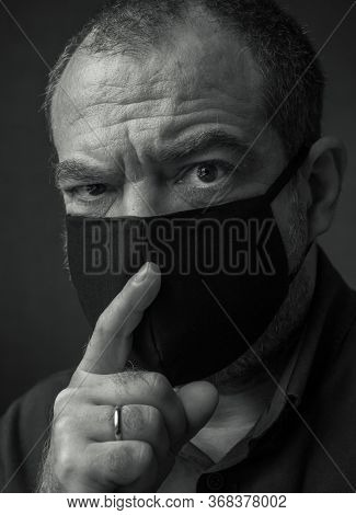 A man in a medical mask with a finger at his mouth. Coronavirus fake news and conspiracy theories concept