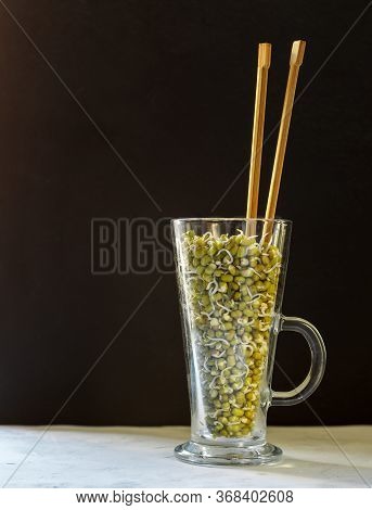 Sprouts Of Munga Beans In A Tall Glass Glass With Wooden Chopsticks On A Dark Background