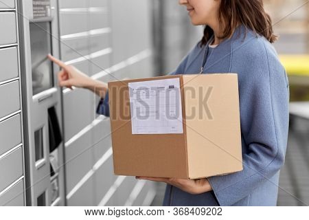 mail delivery and post service concept - close up of happy smiling woman with box at outdoor automated parcel machine choosing operation on touch screen
