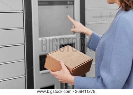 mail delivery and post service concept - close up of happy smiling woman with box at outdoor automated parcel machine choosing operation on touch screen