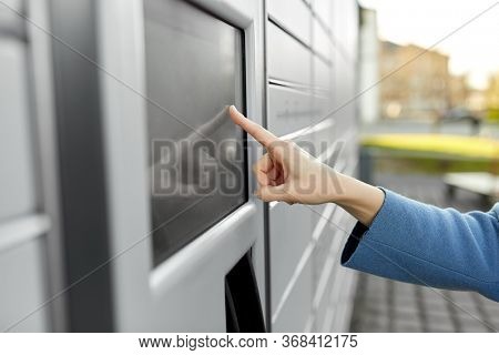 mail delivery and post service concept - close up of woman's hand choosing operation on outdoor automated parcel machine's touch screen