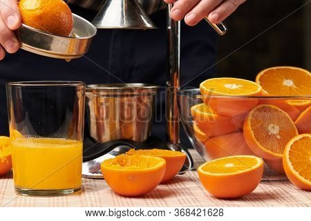 Squeezing an orange with a manual press, close view, making a glass of fresh. Fresh oranges on a wooden table, whole, squeezed and sliced.
