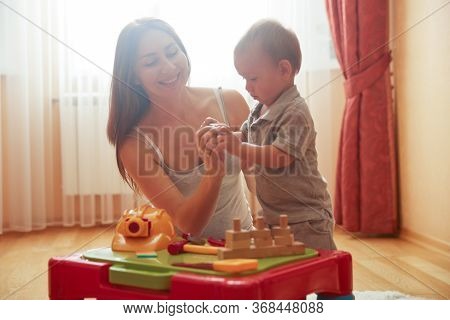 Smiling Happy Young Caucasian Mother Playing With Son Indoor. Caring Nanny Babysitter Teach Child Bo