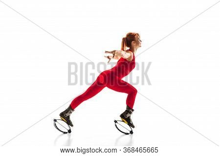 Beautiful Redhead Woman In A Red Sportswear Jumping In A Kangoo Jumps Shoes Isolated On White Studio