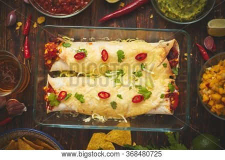 Vegetable Burritos served in glass heatproof dish. With salsa, guacamole, nachos and various ingredients on side. Top view. Tasty mexican homemade food concept.