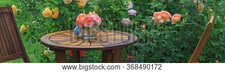 Romantic Sitting Area In The Rose Garden, Round Wooden Table And Chairs Near The Large Flowering Bus