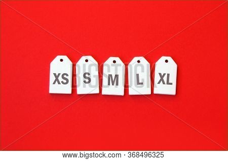 Various Clothing Sizes Xs, S, M, L, Xl On White Wooden Tags On A Red Background.