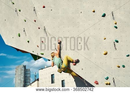 Young Woman Rock Climber Climbing On Artificial Rock Wall In Outside Climbing Gym. Sports Woman Work