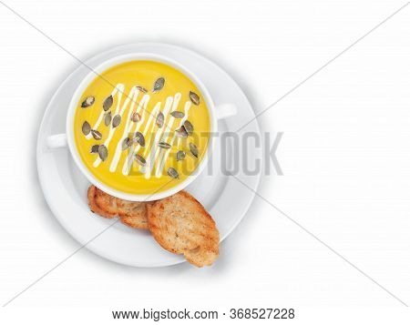 A Bowl Of Pumpkin Soup Garnished With Pumpkin Seeds And Cream, Served With Toasted Bread. View From 