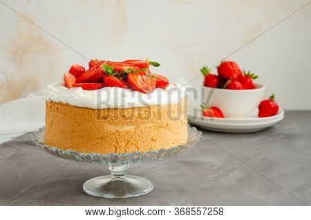 Angel Food Cake With Whipped Cream And Slices Of Fresh Strawberries On Top On A Concrete Background.