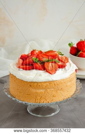Angel Food Cake With Whipped Cream And Slices Of Fresh Strawberries On Top On A Concrete Background.