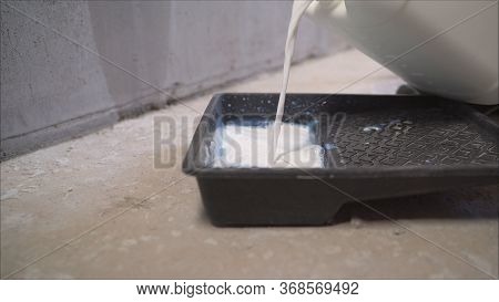 The Primer Is Poured. Wall Primer Mix. A Worker Pours A Primer From A Black Canister. The Worker Pou