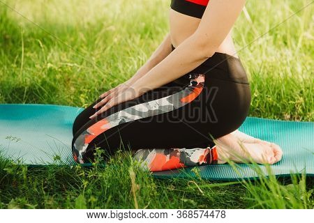 Young Woman Practising Yoga In The Open Air In The Nature On The Grass On The Sunny Day. Outdoor Spo