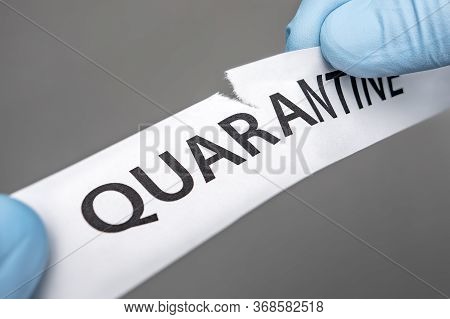 End Of A Coronavirus Quarantine Concept. Hands In Medical Gloves Tearing The Paper With The Word Qua