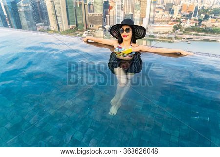 Young woman in a roof top swimming pool, infinity pool with beautiful city view. Vacation in Singapore.