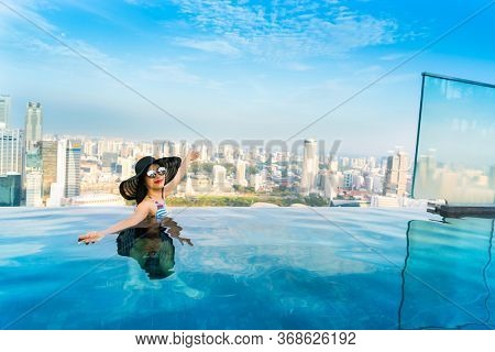 Young woman in a roof top swimming pool, infinity pool with beautiful city view. Vacation in Singapore.
