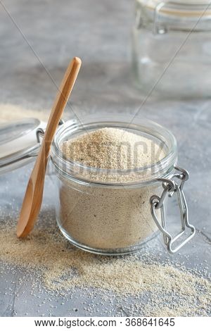 Raw Uncooked Fonio Seeds In A Glass Jar With A Spoon On A Grey Background Close Up