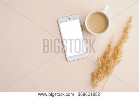 Home Office Desk With Mobile Phone Mockup With Blank Screen, Cup Of Coffee, Dry Flowers On Beige Bac