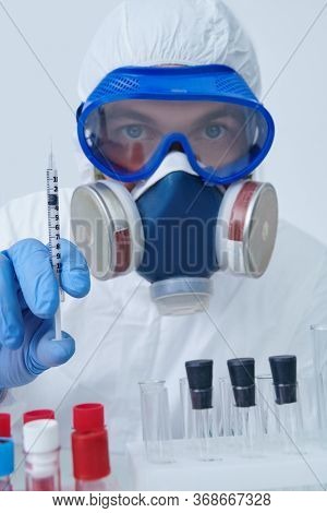 COVID-19. Doctor, microbiologist, scientist in a protective suit, holding a syringe with a vaccine in the laboratory. Coronavirus test.