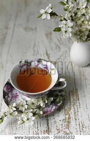 Green Tea In A Cup And Vase With The Branches Of Blossoming Cherry Tree On The Table.