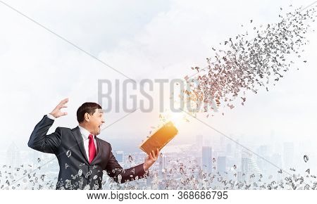 Expressive Businessman Holding Open Book. Emotional Man In Suit Standing On Downtown Background With