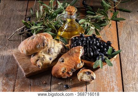 Traditional Italian Puccia Breads With Black Olives On A Cutten Board With Olive Oil And Olive Brach
