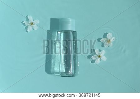 Cosmetic Bottle On Blue Background With Water And Flowers