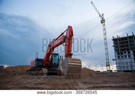 Excavator Working At Construction Site On Earthworks On Evening Sunset. Backhoe Digs Ground For Road