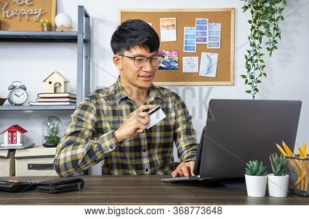 Asian Man Holding Credit Card And Typing Information On Internet With Laptop At Home, Online Shoppin