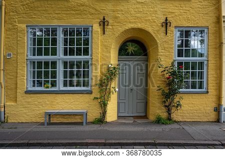 Yellow Facade Of An Historic Old Town House With Muntin Windows And A Door Arch In The Centre Of The