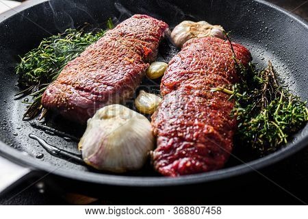 Cooking Denver Steak On Grill Frying Pan With Garlic And Herbs Just From Fire Side View With Smoke
