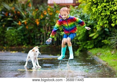 Kids In Puddle In Autumn Rain. Waterproof Wear