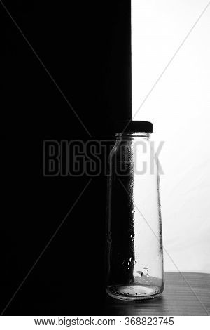 A Small Bottle On A Black And White Background. Half Black And Half White