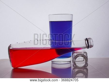 Composition From A Bottle And Glasses With Multicolored Liquid On A White Background. The Bottle Res