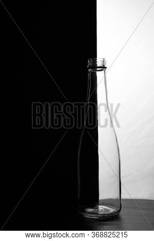 A Small Bottle On A Black And White Background. Half Black And Half White