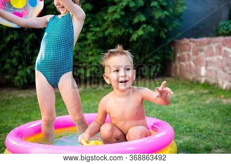 Two Children With Beach Ball At Swimming Pool. Joyful Kid Playing In Inflatable Pool Backyard. Littl