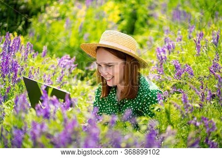 Woman Working On Laptop Sitting In A Field Of Flowers. The Work Of The Freelancer Or Blogger On The 