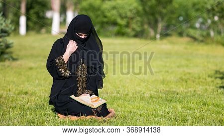 Islamic Woman Prayer In A City Park. Islamic Woman Performs Morning Prayer Sitting On Green Grass In