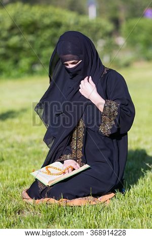 Islamic Woman Prayer In A City Park. Islamic Woman Performs Morning Prayer Sitting On Green Grass A 