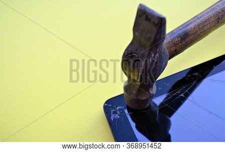 An Old Hammer With A Worn Wooden Handle Hits The Corner Of The Tablet Screen, The Glass Cracks, The 