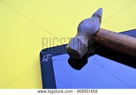 An Old Hammer With A Worn Wooden Lies Next To The Tablet With A Broken Screen, On The Glass Of Which