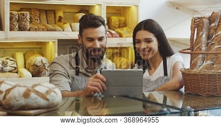 Attractive Male And Female Bread Vendors Scrolling And Watching Something On The Tablet Device While