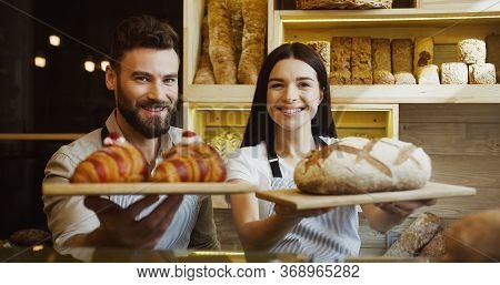 Portrait Of The Two Good Looking Young Smiled Male And Female Bakers Posing With A Bread And Croissa