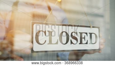 Close Up Of The Male Caucasian Hands Turning A Signboard On The Glass Door Of The Shop From Closed T