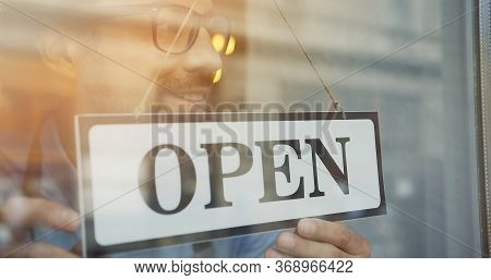 Close Up Of The Male Caucasian Hands Turning A Signboard On The Glass Door Of The Shop From Closed T