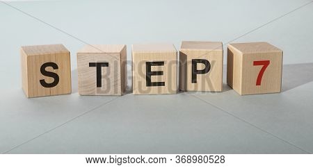 Step By Step Concept. Step 7 Seven Text On Wooden Cube Blocks On Blue Grey Table
